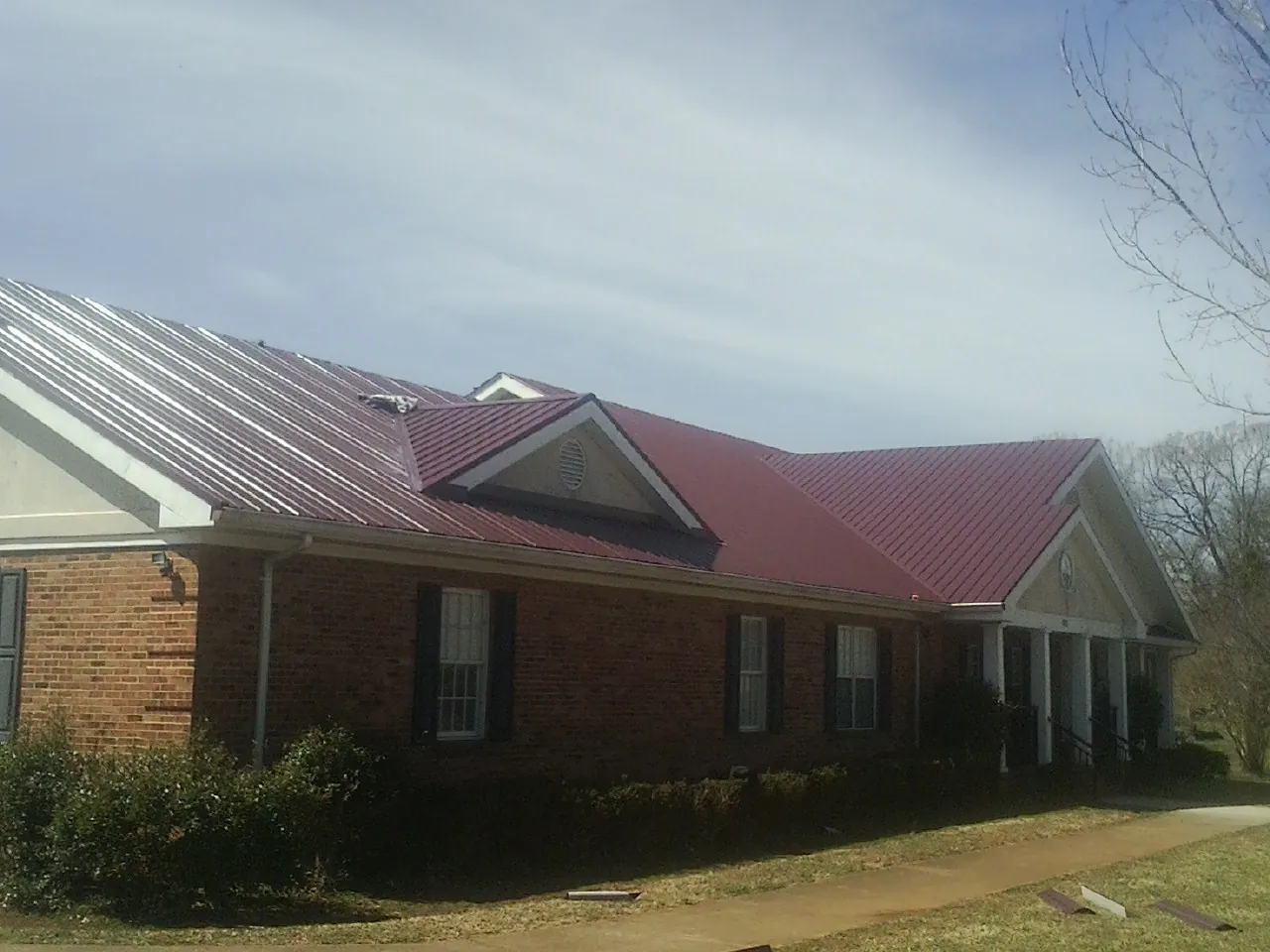 Red metal roof with gabled entries on a long brick building, from a Hail Damage Roof Repair job in Cincinnati