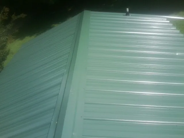 New green metal panels meeting at the ridge of a roof — Flat Roof Repair work by our crew in Cincinnati