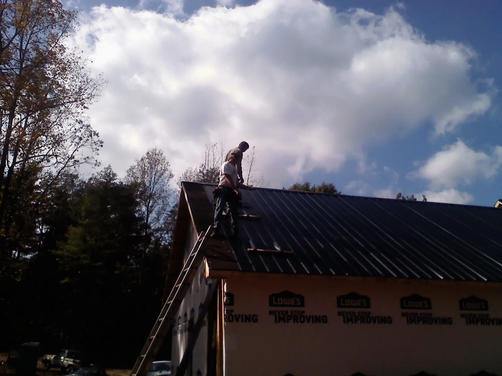 Roofer fastening dark metal panels high against a cloudy sky, from a Roof Inspection job in Cincinnati