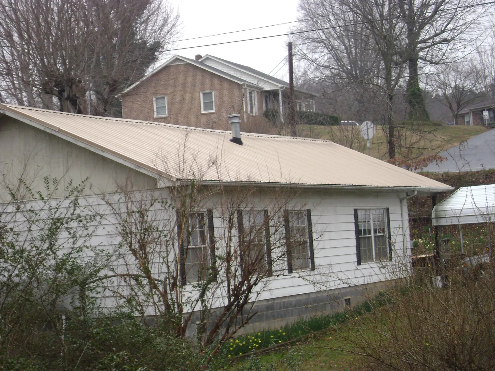 Tan metal roof on a white sided house set into a hillside — Commercial Roofing by Roofing Brothers in Cincinnati